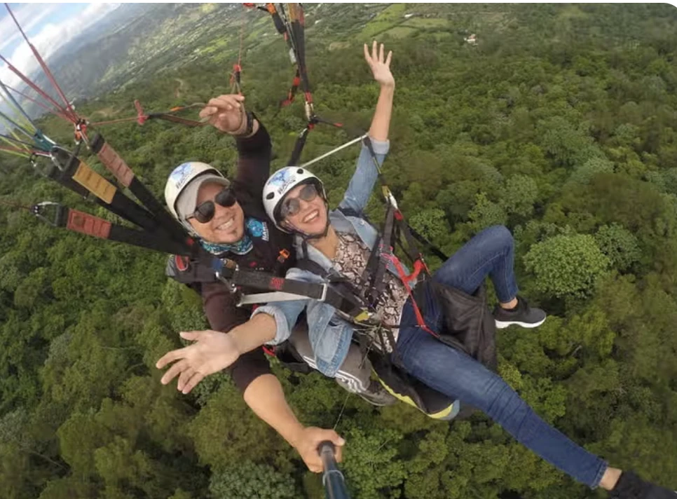 Dos personas en parapente sobre un valle arbolado