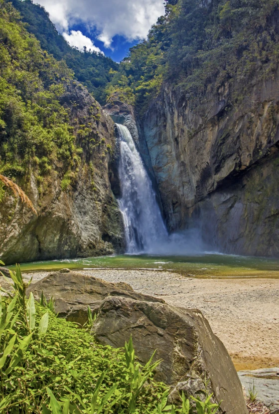 Waterfall cascading between rocky cliffs into a pool, with trees and boulders